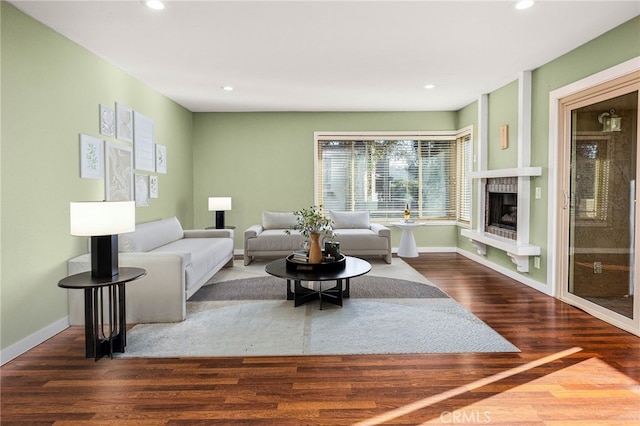 living area featuring a fireplace with raised hearth, baseboards, wood finished floors, and recessed lighting