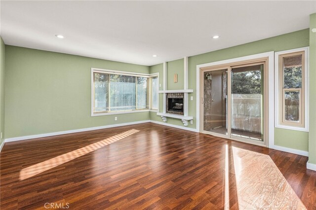 unfurnished living room with baseboards, a fireplace with raised hearth, wood finished floors, and recessed lighting