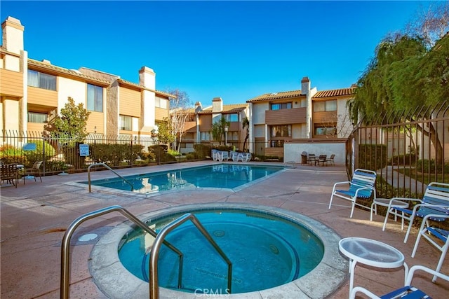 view of swimming pool featuring a community hot tub, a patio, fence, and a residential view