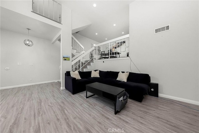 living area featuring baseboards, visible vents, stairway, wood finished floors, and a high ceiling