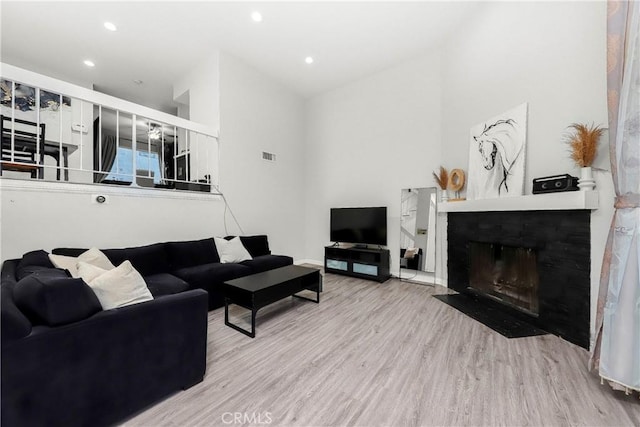 living area with a fireplace with flush hearth, recessed lighting, visible vents, and wood finished floors