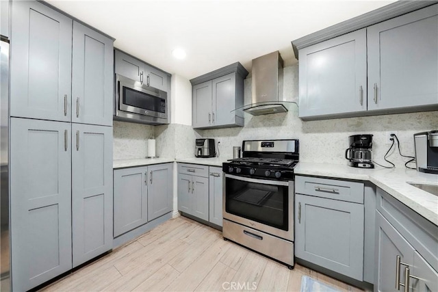 kitchen with stainless steel appliances, light wood-style floors, wall chimney range hood, gray cabinets, and tasteful backsplash