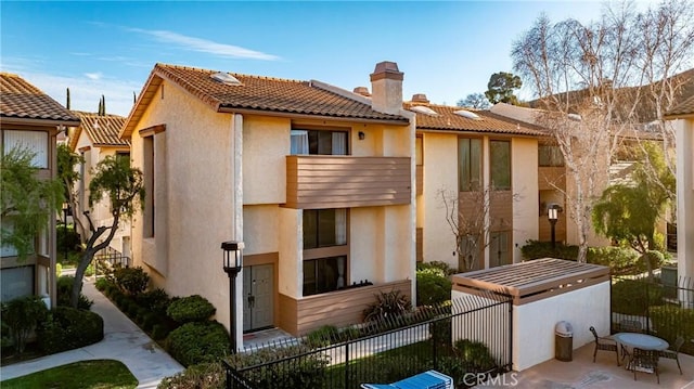 back of property featuring a patio, a chimney, a tiled roof, fence, and stucco siding