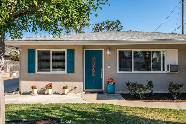 bungalow-style house with stucco siding, roof with shingles, fence, cooling unit, and a front yard