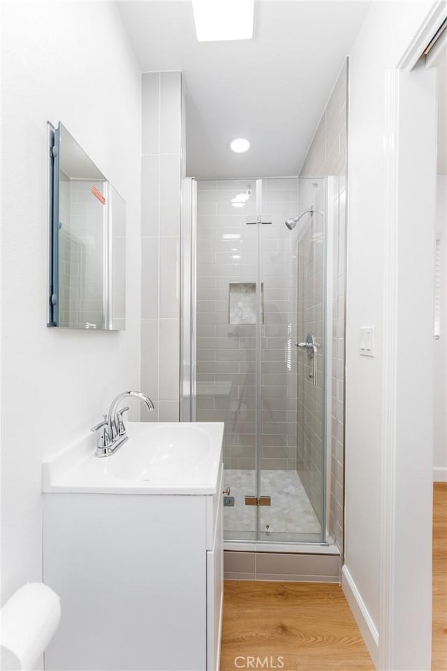 full bath with a stall shower, vanity, baseboards, and wood finished floors