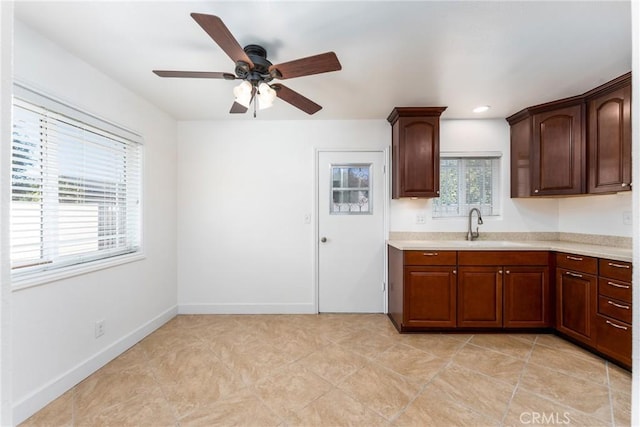 kitchen featuring light countertops, a sink, a ceiling fan, and baseboards