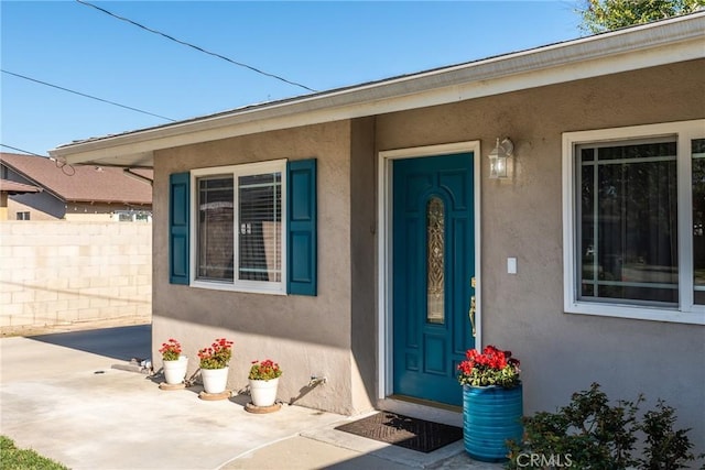 view of exterior entry featuring a patio area, fence, and stucco siding