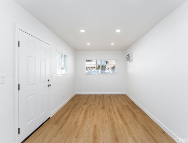 empty room with light wood finished floors, a wall mounted air conditioner, baseboards, and recessed lighting