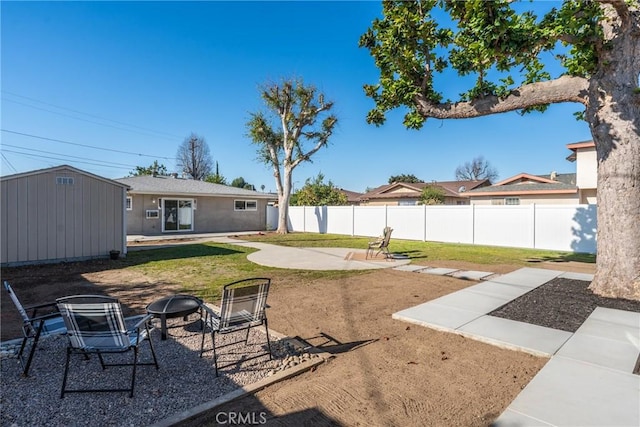 view of yard featuring a storage unit, a patio area, fence, an outdoor structure, and a fire pit