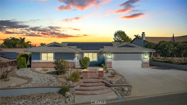 single story home featuring concrete driveway, brick siding, an attached garage, and solar panels