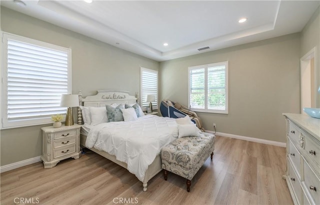 bedroom featuring light wood finished floors, baseboards, and a raised ceiling