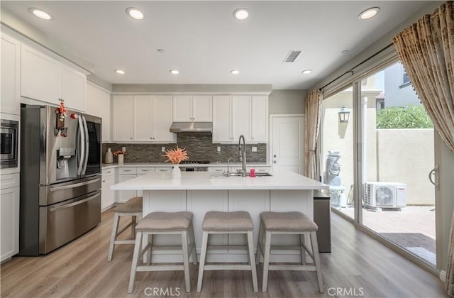 kitchen with visible vents, a center island with sink, appliances with stainless steel finishes, and light countertops