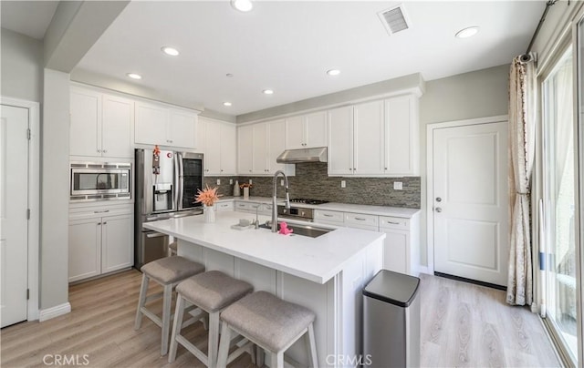 kitchen with a breakfast bar area, under cabinet range hood, stainless steel appliances, visible vents, and light countertops