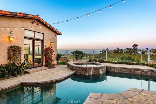 pool at dusk featuring a patio, an in ground hot tub, fence, french doors, and an outdoor pool