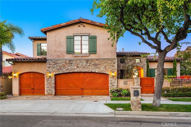 mediterranean / spanish house featuring stone siding, an attached garage, a tile roof, and stucco siding