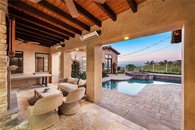 pool at dusk featuring a ceiling fan, a pool with connected hot tub, and a patio area