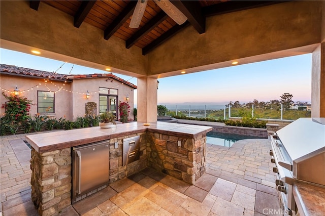 patio terrace at dusk featuring exterior kitchen and an outdoor pool