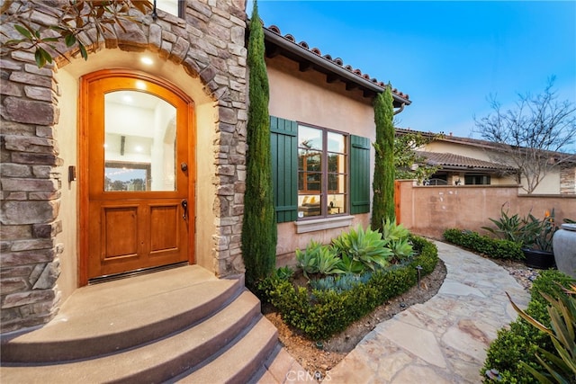 doorway to property featuring stone siding, fence, and stucco siding