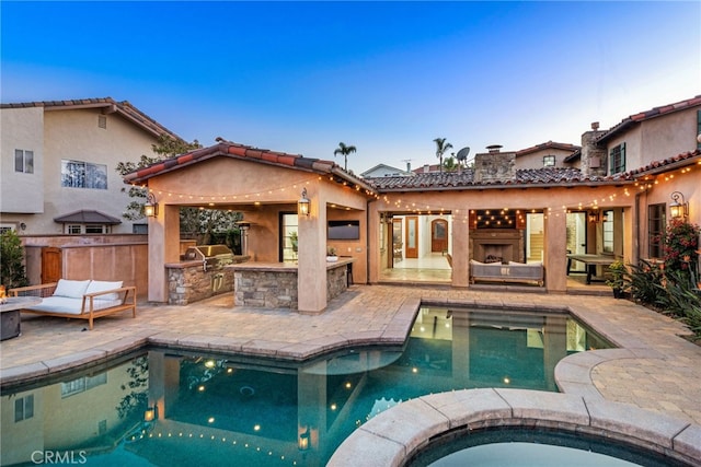 rear view of property featuring a fireplace, stucco siding, a patio area, an in ground hot tub, and exterior kitchen