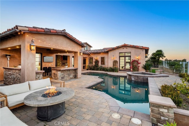 pool at dusk featuring french doors, a pool with connected hot tub, a patio area, fence, and a fire pit