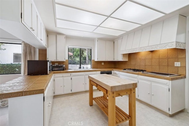 kitchen with tile countertops, light floors, backsplash, white cabinetry, and a sink