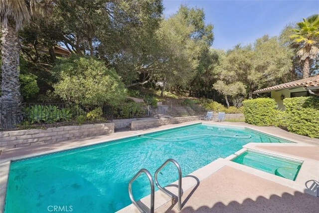 view of swimming pool with a pool with connected hot tub, fence, and a patio