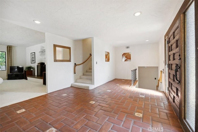 entrance foyer with brick floor, recessed lighting, visible vents, and stairs