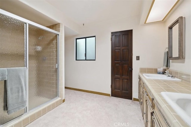 bathroom with double vanity, a stall shower, baseboards, and a sink