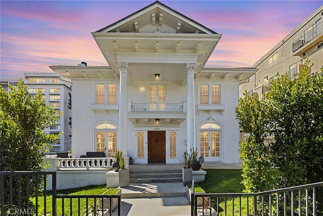 neoclassical home with french doors, fence, a balcony, and stucco siding