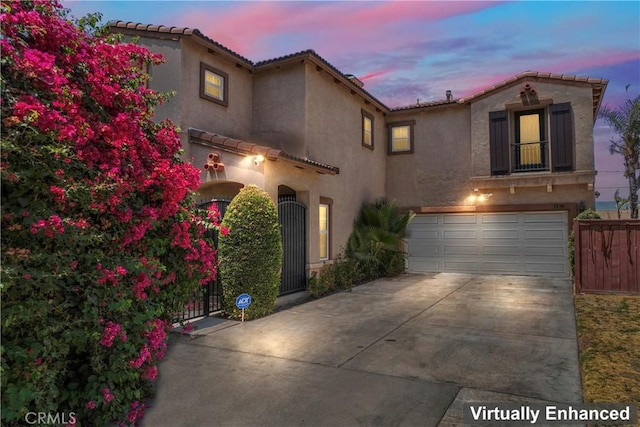 mediterranean / spanish-style home with concrete driveway, a tile roof, an attached garage, fence, and stucco siding