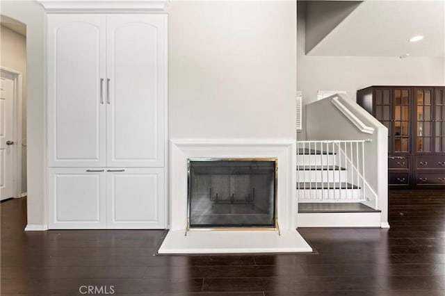 unfurnished living room with stairs, a glass covered fireplace, and wood finished floors