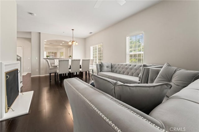 living area with a fireplace with raised hearth, dark wood-style flooring, a chandelier, and baseboards