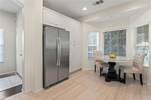 kitchen featuring visible vents, baseboards, freestanding refrigerator, and white cabinetry