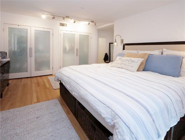 bedroom with french doors, light wood finished floors, rail lighting, and visible vents