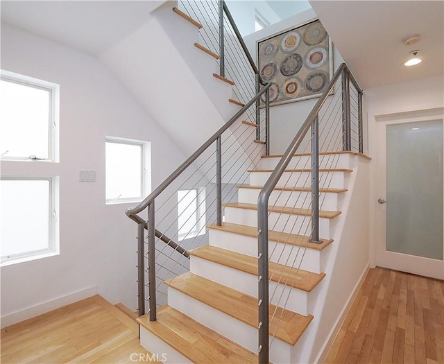 stairway with lofted ceiling, wood finished floors, and baseboards