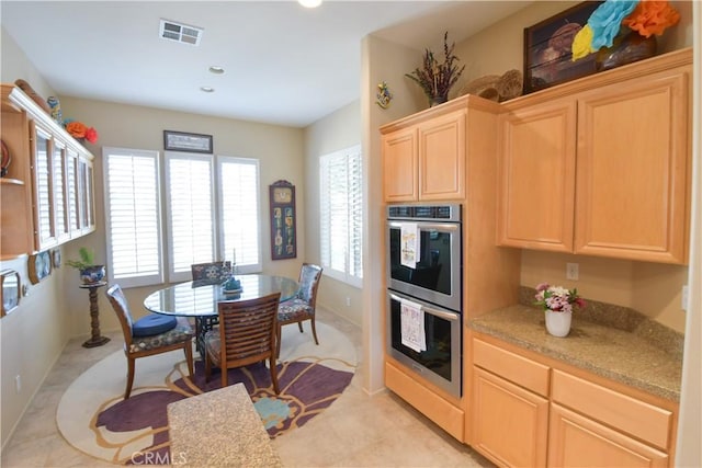 kitchen featuring double oven, light countertops, light brown cabinets, and visible vents