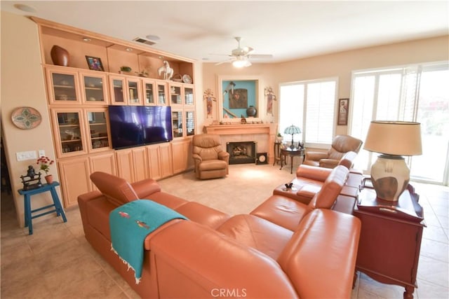 living room featuring light tile patterned floors, visible vents, a ceiling fan, and a tile fireplace