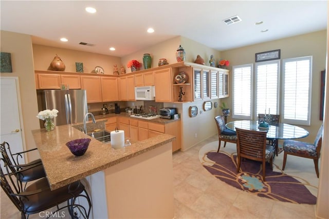 kitchen featuring light brown cabinets, recessed lighting, white appliances, a sink, and visible vents