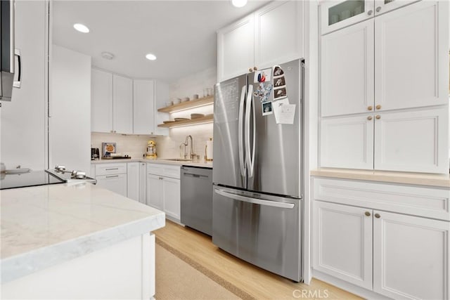 kitchen with light stone counters, stainless steel appliances, a sink, white cabinets, and light wood-type flooring