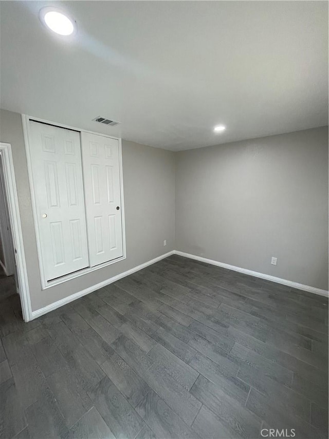 unfurnished bedroom with dark wood-style floors, visible vents, and baseboards