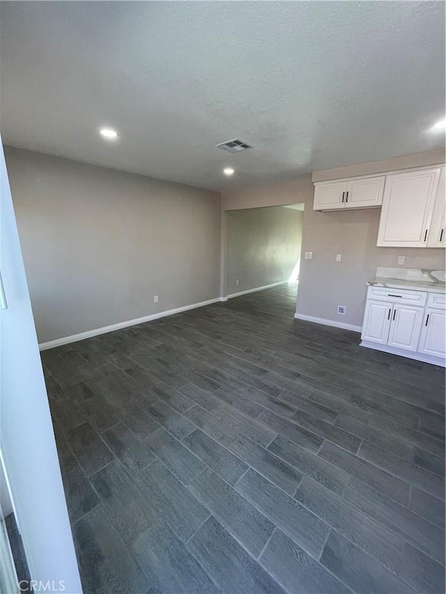 interior space with a textured ceiling, recessed lighting, visible vents, baseboards, and dark wood finished floors