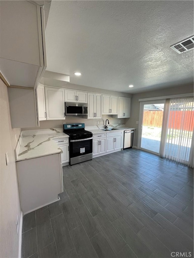 kitchen featuring visible vents, white cabinets, appliances with stainless steel finishes, dark wood-style flooring, and a sink