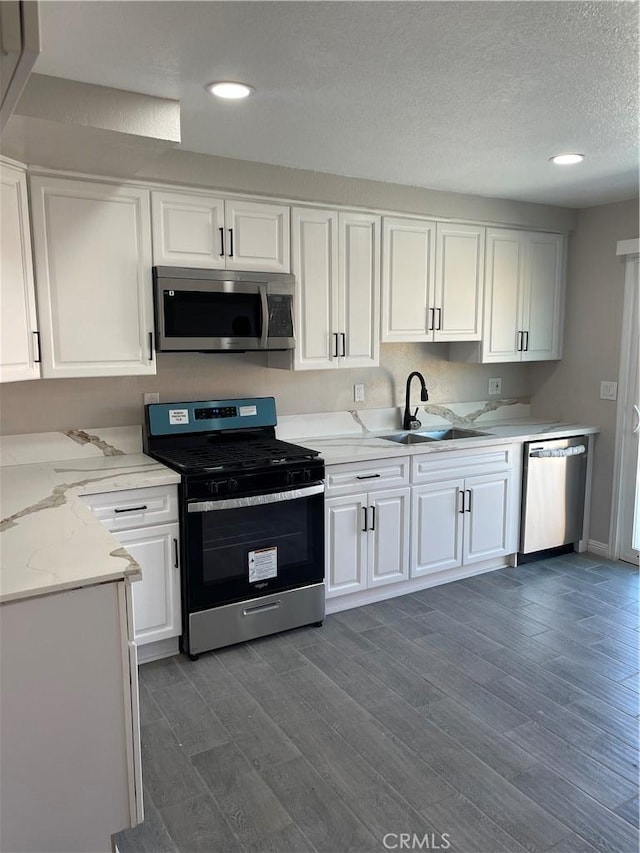 kitchen featuring white cabinets, dark wood finished floors, light stone countertops, stainless steel appliances, and a sink