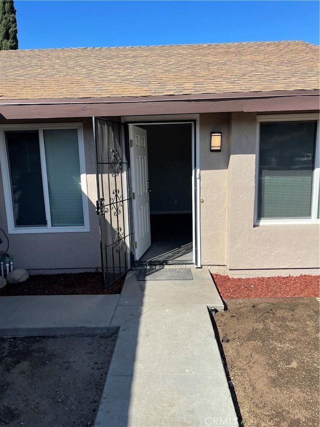 view of exterior entry with stucco siding and roof with shingles