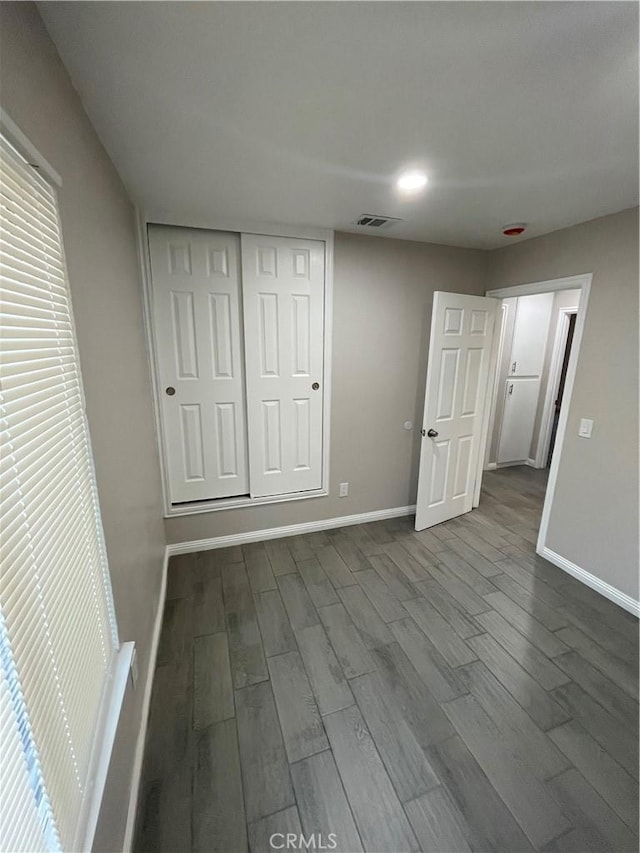 unfurnished bedroom featuring baseboards, a closet, visible vents, and wood finished floors