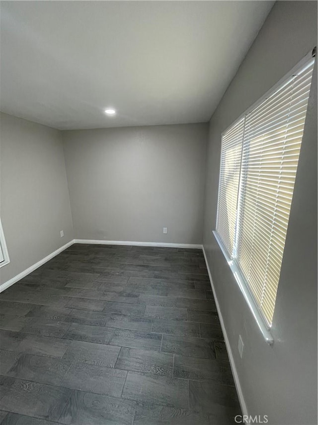 spare room with baseboards and dark wood-type flooring