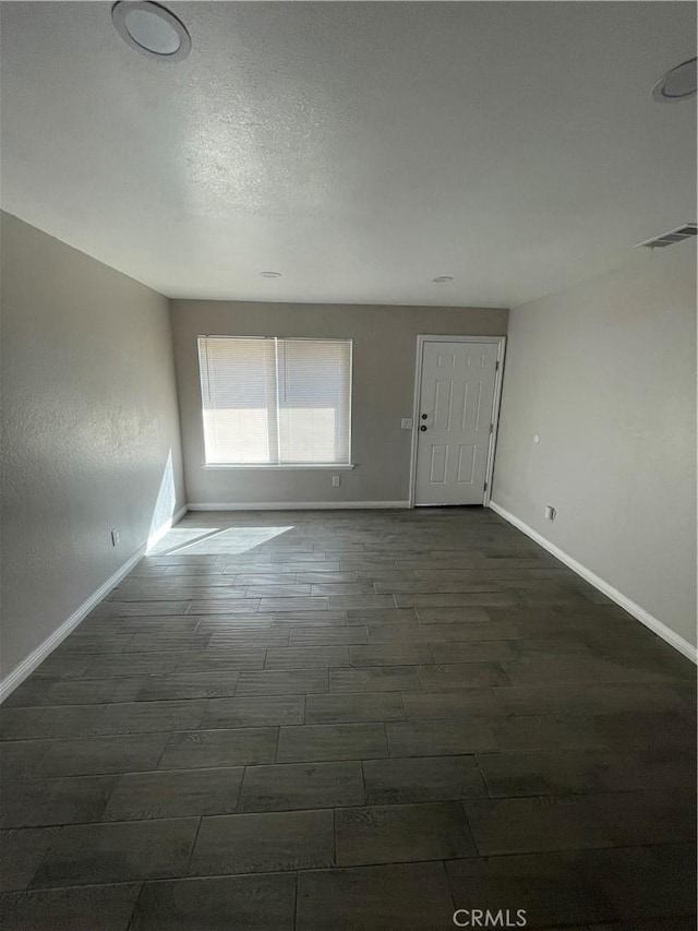 empty room featuring dark wood-style flooring, visible vents, a textured ceiling, and baseboards