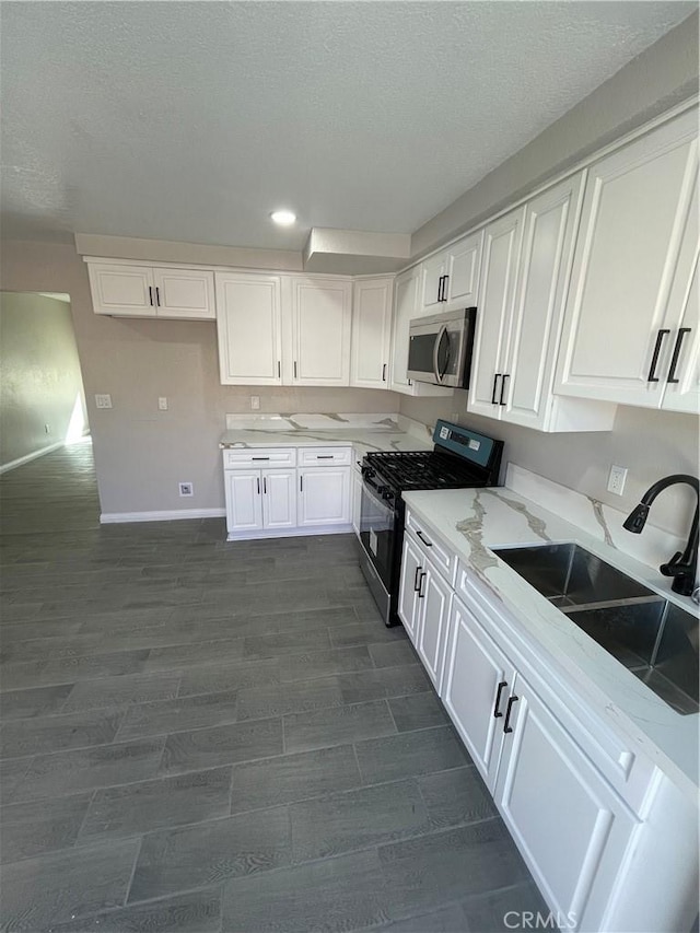 kitchen featuring light stone counters, dark wood-type flooring, a sink, white cabinets, and appliances with stainless steel finishes