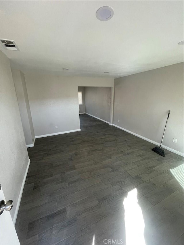 unfurnished room with dark wood-type flooring, visible vents, and baseboards