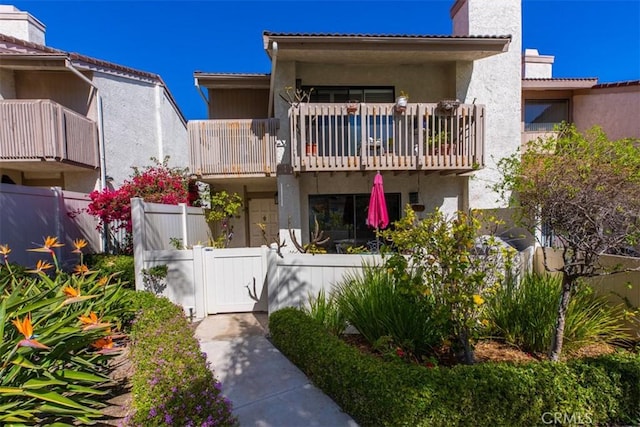 view of front of home featuring a balcony, a fenced front yard, a chimney, and stucco siding